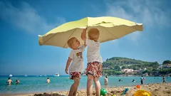 Due bambini sotto un ombrellone giallo sulla spiaggia al mare