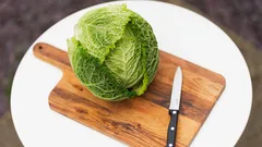Verza verde su tagliere di legno con coltello affilato su tavolo bianco