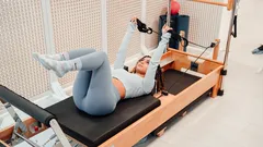 Donna che fa esercizi Pilates su macchina Reformer in palestra moderna