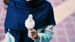 Persona con sciarpa blu che tiene un cono di gelato soft serve bianco