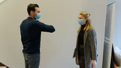 Due persone con mascherine che si salutano con il gomito mantenendo distanza sociale