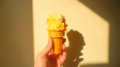 Mano che tiene cono gelato giallo con sfondo di muro e ombra